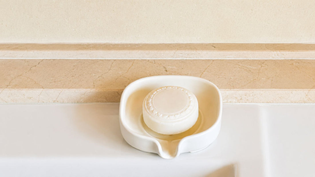 Ceramic self draining soap dish with natural bar soap on a bathroom sink, handmade ceramic soap holder for a modern eco-friendly bathroom.