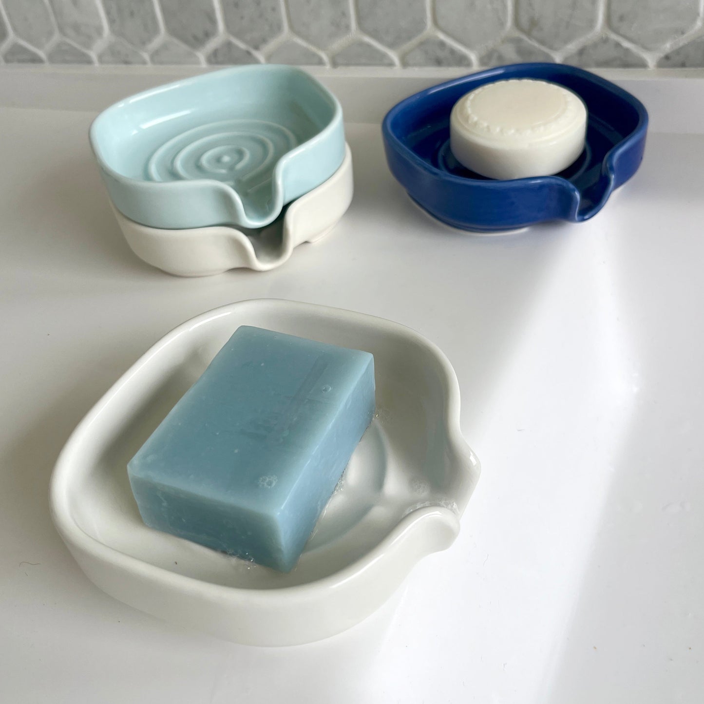 Four soap dishes with bars of soap on a bathroom counter