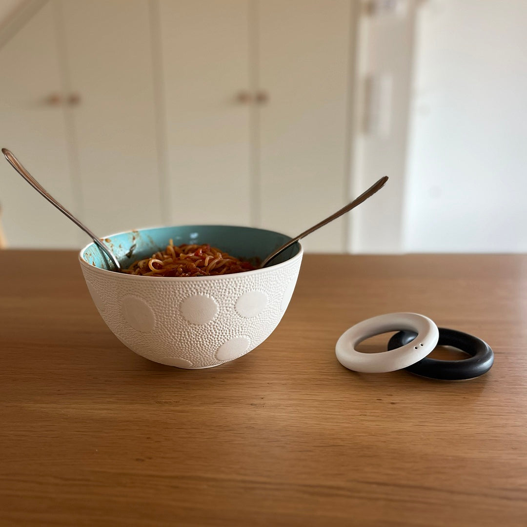 Lifestle photo with bowl and a set a black and white salt and pepper shaker rings.High-fired and food-safe, this modern minimalist design makes an elegant wedding favour or anniversary gift for design-conscious couples.
